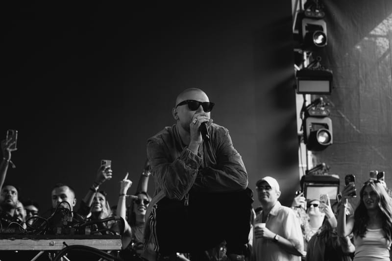Ali Love crouching at the front of a festival stage, singing, in black and white