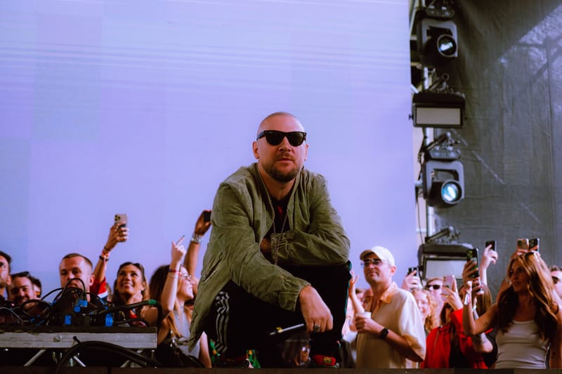 Ali Love crouching at the front of a festival stage, the crowd behind him