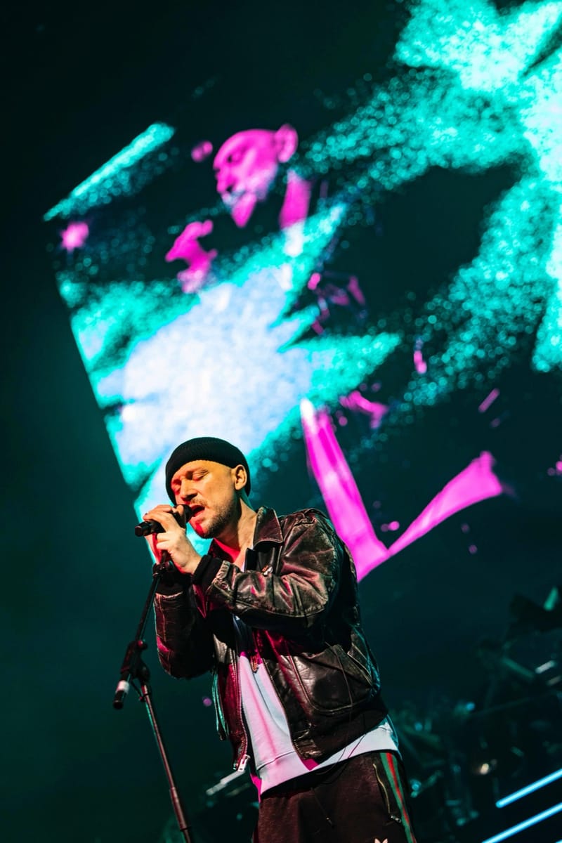 Ali Love singing at a microphone stand, teal and pink light behind him