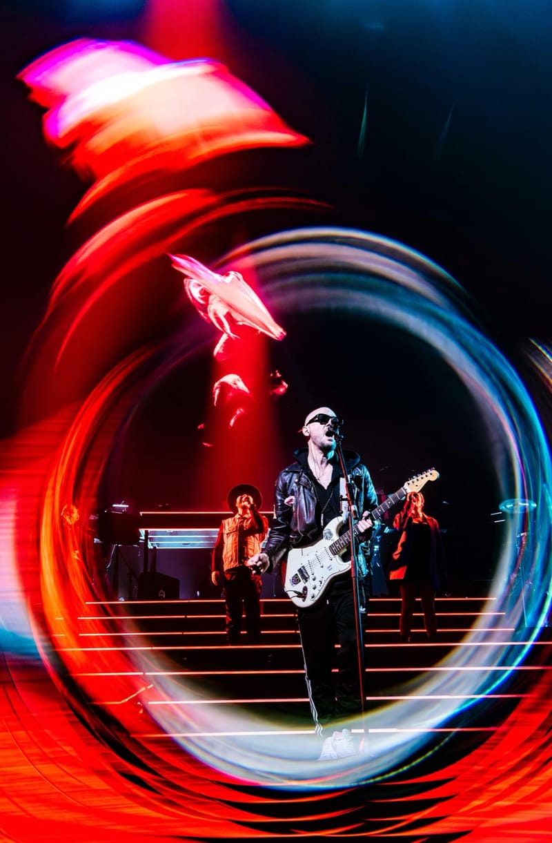 Ali Love with a white guitar, framed by a swirl of red and blue light