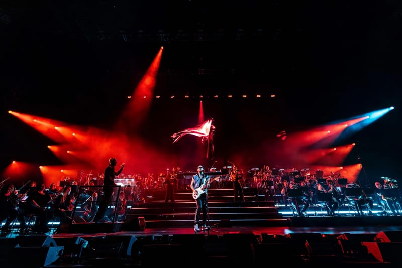 Ali Love with a guitar on an orchestral stage under red and blue lights