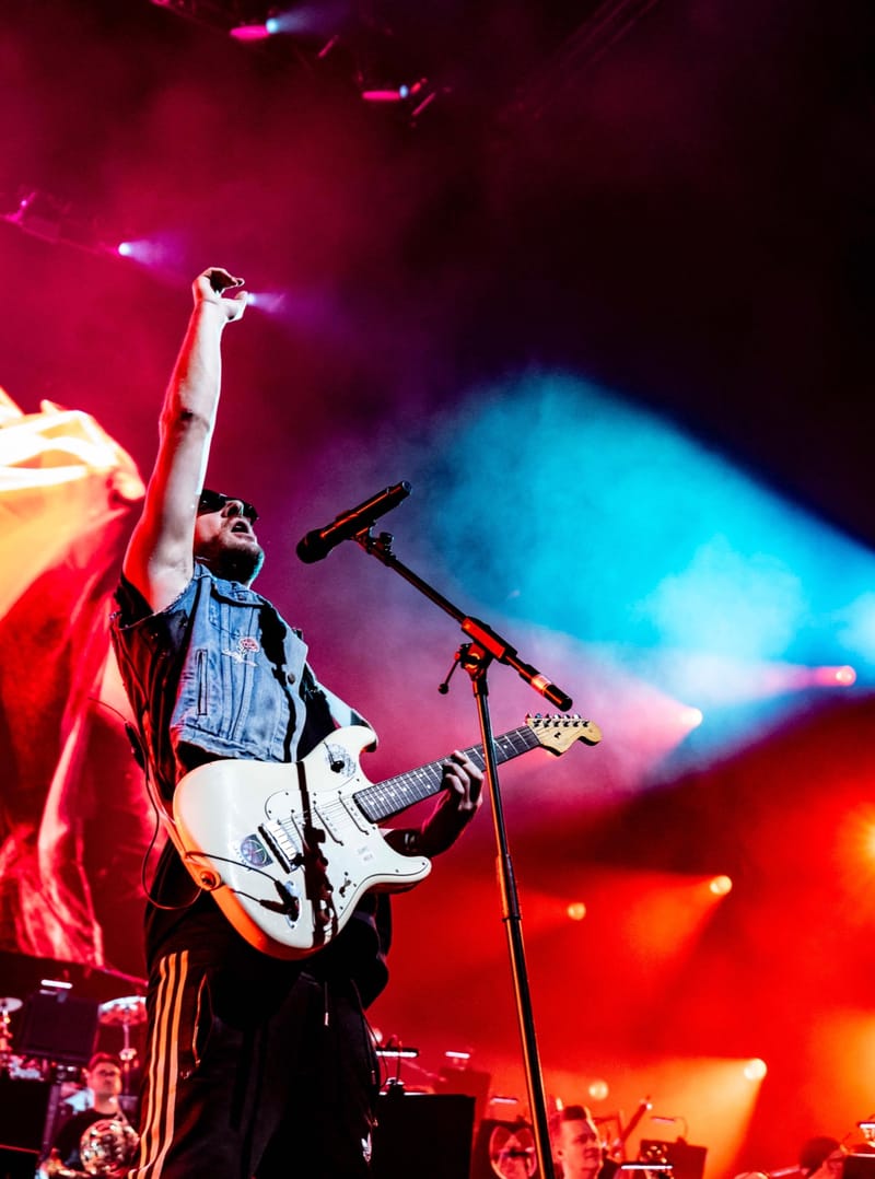 Ali Love raising his fist on stage with a white guitar, under red and blue lights