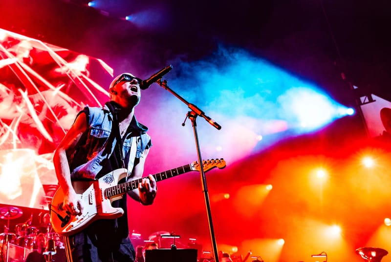 Ali Love singing and playing a white guitar under red stage lights