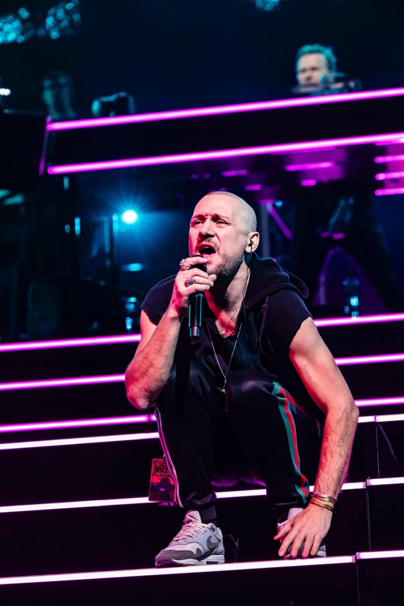 Ali Love crouching on lit stage steps, singing into a microphone